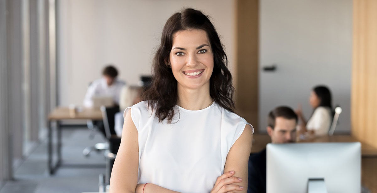 1. A woman in a white shirt stands confidently in front of a desk, engaged in a professional setting.