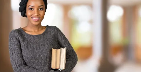 A female student standing comfortably while holding two books and preparing for study.